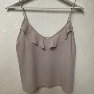 Beige linnetopp från Gina Tricot - Säljer beige linnetopp från Gina Tricot, stl XS 💕Toppen har tunna axelband och en söt volangdetalj framtill. Nästan aldrig använd så är i jättebra skick!