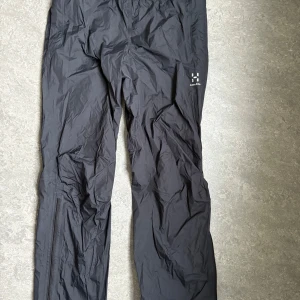Svarta regnbyxor skalbyxor från Haglöfs - Säljer ett par svarta skalbyxor från Haglöfs i storlek XL för dam. Byxorna är perfekta för utomhusaktiviteter och har en praktisk design med dragkedja. De är tillverkade i ett slitstarkt material som passar bra för olika väderförhållanden. Storlek:XL. Irginalpris ca 1300kr.