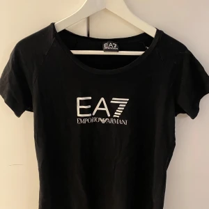 Svart t-shirt från Emporio Armani - Snygg svart t-shirt från Emporio Armani med EA7-logga i vitt på bröstet. Perfekt för en stilren look. Kortärmad och tillverkad i mjukt material för extra komfort.