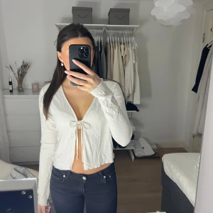 Vit ribbad knytblus - Säljer en stilren vit ribbad blus från veromoda med knytning framtill. Blusen har långa ärmar och en v-ringad design som ger en elegant touch. Perfekt för både vardag och speciella tillfällen.