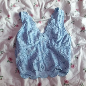 Blå spetslinne - Säljer ett vackert blått spetslinne med blommigt mönster. Linnet har en v-ringad design och är perfekt för sommarens varma dagar. Detaljerna i spetsen ger en romantisk känsla. Passar bra till både jeans och kjol.