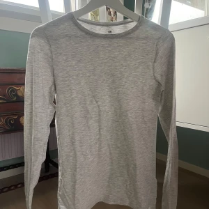 Grå långärmad tröja från H&M - Säljer en stilren grå långärmad tröja från H&M. Perfekt för en avslappnad look och enkel att matcha med andra plagg. Tröjan har en rund halsringning och är tillverkad i ett mjukt material.