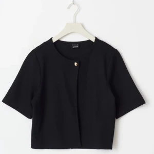 Svart kortärmad topp från Gina Tricot  - Snygg svart kortärmad topp från Gina med en enkel knappdetalj framtill. Jackan har en croppad passform och är tillverkad i ett mjukt material. Lappen är kvar och det är storlek m men sitter som s! Skriv till mig innan ni trycker på köp nu❤️