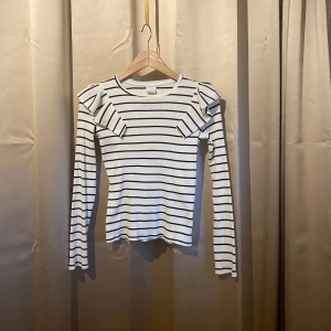 Randig långärmad topp från Zara - Säljer en stilren randig topp från Zara i vitt och svart. Toppen har långa ärmar och volangdetaljer vid axlarna som ger en extra touch. Perfekt för en trendig look!