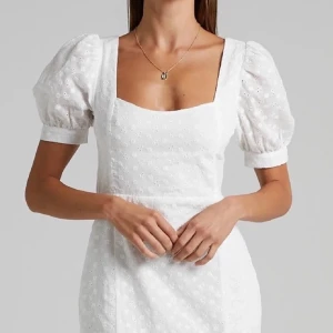 Vit klänning med puffärmar - Charmig vit klänning med puffärmar och fyrkantig urringning. Klänningen har en söt broderad design och en liten slits framtill. Baksidan har en öppen rygg med knytband för en extra detalj. Perfekt för student! Den är ny med prislapp på! 