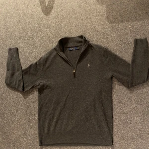 Grå tröja från Polo Ralph Lauren - Säljer en stilren grå tröja från Polo Ralph Lauren med dragkedja vid halsen. Tröjan har långa ärmar och en broderad logotyp på bröstet. Perfekt för en klassisk och avslappnad look. Storlek S