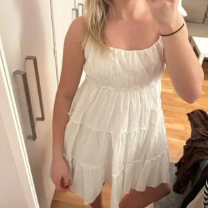 Vit kortklänning med volanger - Söt vit kortklänning med volanger och smala axelband. Perfekt för varma sommardagar. Klänningen har en luftig passform och är aldrig använd.