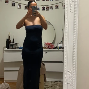 Mörkblå axelbandslös klänning - Säljer en elegant mörkblå axelbandslös klänning som sitter tight och smickrande. Perfekt för en kväll ute eller en speciell tillställning. Klänningen har en stilren design som framhäver figuren. Har även en slits bakifrån 