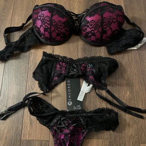 Svart och rosa spetsunderklädesset - Elegant underklädesset i svart och rosa från Censored. Setet består av en bh med vadderade kupor och spetsdetaljer samt matchande trosor med snörning. Perfekt för en speciell kväll. Aldrig använd
