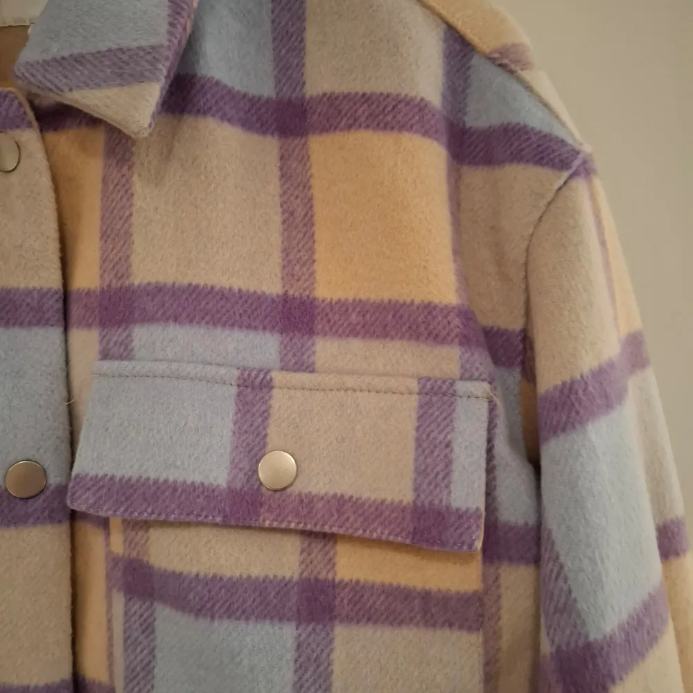 Säljer en snygg rutig overshirt från Vila i pastellfärger. Jackan har en kombination av beige, lila och blå rutor. Den är långärmad med knappar framtill och två bröstfickor med lock. Perfekt för lager-på-lager-stil!. Takit.