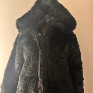 Svart pälsjacka  - Säljer en snygg svart pälsjacka från Monki med huva. Jackan har en mjuk och fluffig. Den är lång och varm, perfekt till kalla dagar.