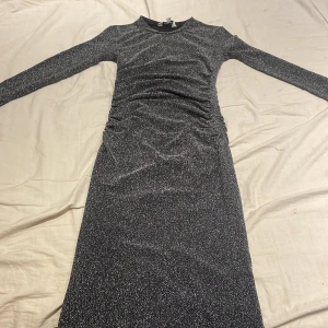 Glittrig svart klänning från Kappahl - Snygg glittrig svart klänning från Kappahl i storlek XS. Klänningen har en figurnära passform och långa ärmar, perfekt för en kväll ute. Den glittriga ytan ger en festlig touch. Passar utmärkt för speciella tillfällen.