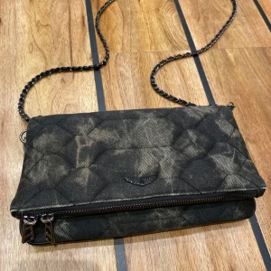 Svart quiltad axelväska med kedja - Snygg svart quiltad axelväska med kedja och dragkedja. Perfekt för att ge din outfit en edgy touch. Den har en stilren design med en diskret logga framtill.