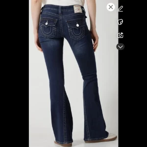 Mörkblå True Religion bootcut jeans - Snygga mörkblå bootcut jeans med låg midja och klassisk femficksdesign. Jeansen har dekorativa sömmar på bakfickorna och en lätt slitning framtill för en trendig look. Passar mig som har 36 och är 170 samma jeans på alla bilder är mina. Är lagade i skrevet inget man ser om man har på sig byxorna på grund av placeringen pm för bilder🤍 midjemått rakt över är 39 och innerbenslängd är ca 80