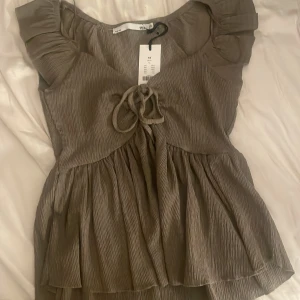 Beige topp från 157 - Säljer en söt beige topp från 157 i storlek XS. Toppen har korta ärmar och en knytning framtill som ger en fin detalj. Ses även som en blus