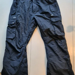 Svarta vinterbyxor från Dope - Säljer ett par svarta vinterbyxor från Dope, modell Iconic.. Byxorna har flera praktiska fickor med knappar och är tillverkade i 100% polyester med nylonfoder. Perfekta för kyligare väder med sin robusta design.