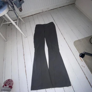 Grå byxor från Gina Tricot - Snygga grå kostym byxor från Gina Tricot i storlek XS. Byxorna har en utsvängd bootcut som ger en trendig look. Perfekta för att skapa en classy outfit. Sömmen längst ner vid fötterna har blivit uppsplittrad så byxorna blev längre, men för mig är inte de ett problem😌