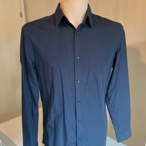 Mörkblå skjorta från H&M - Snygg mörkblå skjorta från H&M i slim fit. Skjortan har långa ärmar och knappar framtill. Easy iron. Perfekt för en stilren look.