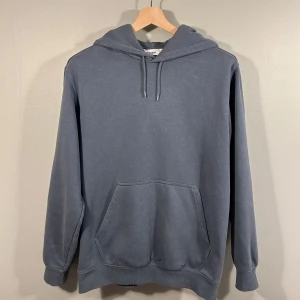 Weekday Grå/Blå Hoodie - Säljer en stilren grå hoodie från Weekday i storlek M. Den har en klassisk design med känguruficka och justerbar huva med dragsko. Perfekt för en avslappnad look. Passar även storlek S. Nyskick! Nypris runt 599kr.