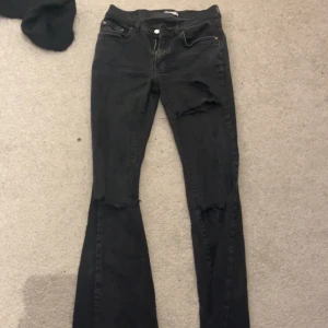 Lågmidjade jeans - Snygga svarta jeans med slitningar på låren och knäna. De har en klassisk femficksdesign och knappar i midjan. Perfekta för en avslappnad stil med en edgy touch.