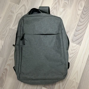 Grå ryggsäck med USB-port - Snygg och praktisk grå ryggsäck med inbyggd USB-port för enkel laddning av dina enheter. Ryggsäcken har justerbara axelremmar och flera fack för optimal förvaring. Perfekt för både skola och arbete.