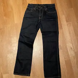 Snygga blå  jeans från Nudie Jeans med klassisk femficksdesign och kontrasterande sömmar. Perfekta för en stilren look. De har en knappgylf och är tillverkade i slitstarkt denim. Storlek 31/32
