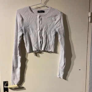 Vit ribbad kofta från FB Sister - Säljer en vit ribbad kofta från FB Sister. Den är croppad med långa ärmar och har en stilren design. Perfekt för lager-på-lager eller som ett lättare plagg under kyligare dagar.