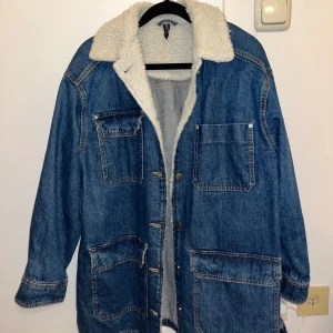 Blå jeansjacka med teddyfoder - Blå jeansjacka med mysigt vitt teddyfoder. Oversized passform med stora fickor och knappar framtill. Passar till höst/vår. Använd 1 gång, jättebra skick