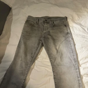 Grå jeansbyxor från G-Star RAW strl 34 - Snygga grå jeansbyxor från G-Star RAW med klassisk femficksdesign. Byxorna har en rak passform och är tillverkade i ett slitstarkt material. Perfekta för en avslappnad stil. Strl 34