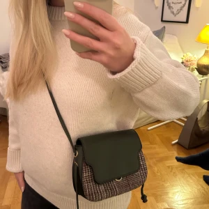 Crossbody väska med mönstrad detalj - Snygg axelväska med en kombination av mörkgrönt lock och mönstrad kropp. Väskan har en justerbar axelrem och en praktisk storlek för vardagsbruk. 