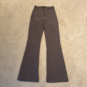 Grå kostym byxa från Gina Tricot - Snygga grå byxor från Gina Tricot i en högmidjad modell. Byxorna har en bootcut-stil som ger en trendig look. Perfekta för att skapa en stilren outfit. Har gått en tråd på dna knät.