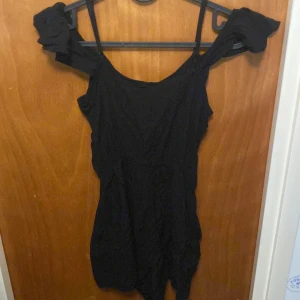 Svart offshoulder klänning - Snygg svart offshoulder klänning med volangdetaljer på axlarna. Perfekt för en kväll ute eller en speciell tillställning. Klänningen har en elegant och stilren design som framhäver axlarna.