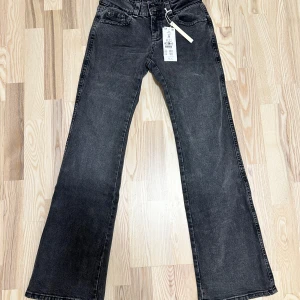 Svarta bootcut jeans - Snygga svarta bootcut jeans med låg midja och klassisk femficksdesign. Jeansen har en dragkedja och knapp framtill samt dekorativa bakfickor med knappar. Perfekta för en stilren look. Är i nyskick!