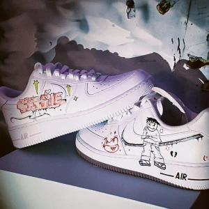 Nike air force 1 - Snygga vita Nike Air Force sneakers med handmålade motiv. Ena skon har en blå fjäril och texten 'HEAVEN', medan den andra har en tecknad figur och texten 'LOVE'. Perfekta för dig som vill sticka ut med en personlig stil.