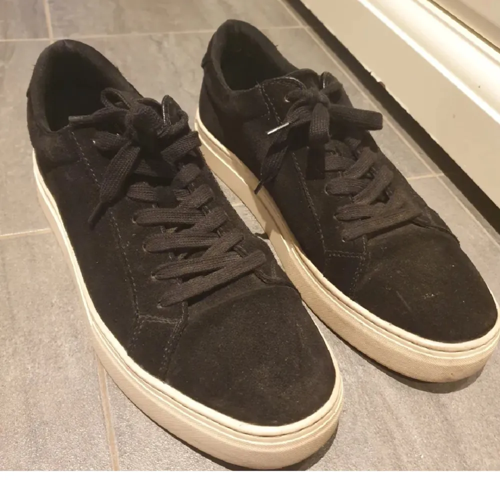 Snygga svarta sneakers i mocka med vit sula och klassisk snörning. Perfekta för en stilren look.. Kengät.