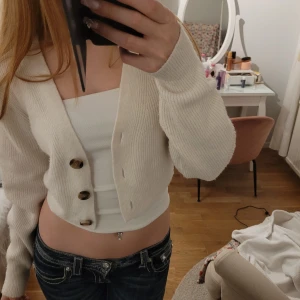 Beige kofta från H&M - Säljer en stilren beige kofta i storlek S från H&M med stora knappar framtill. Koftan är ribbad och har långa ärmar och endast använd få gånger. Passar bra till både jeans och kjol. Säljer även tubtoppen på bilden💕