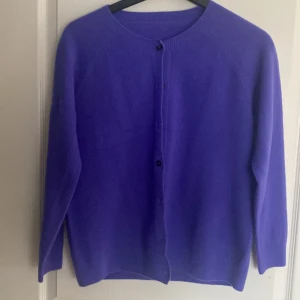 Lila kofta med knappar - Säljer en stilren lila kofta med knappar framtill. Koftan har långa ärmar och en rund halsringning, perfekt för att hålla dig varm och snygg under kyligare dagar. Ett måste i garderoben för dig som älskar färg!