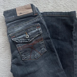 Grå jeans från LTB Industries - Snygga grå jeans från LTB Industries med unika sömmar och knappar på bakfickorna. De har en klassisk femficksdesign och en lätt utsvängd bootcut-stil. Perfekta för en avslappnad look.