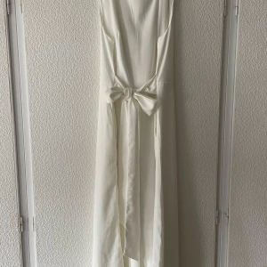 Vit byxdress från Vila  - En vit byxdress från Vila i storlek 44. Den är aldrig använd och har prislappen kvar. Den har band från sidorna som går att knyta både fram och bak. Det är en kroppar modell, alltså är byxbenen inte ända ner till fötterna.