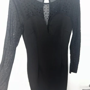 Svart klänning från Betsey Johnson - Säljer en elegant svart klänning från Betsey Johnson. Den har långa ärmar med prickigt mönster i mesh och en snygg v-ringad detalj framtill. Perfekt för festliga tillfällen! ✨I nyskick och sitter jätte fint.