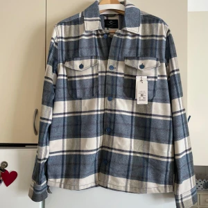 Rutig overshirt från Cubus - Säljer en snygg rutig overshirt från Cubus i blått och vitt. Den har långa ärmar och knappar framtill. Perfekt för höst och vår, och den är både vattenavvisande och andas bra tack vare Bionic Finish Eco. Helt ny med taggar kvar!