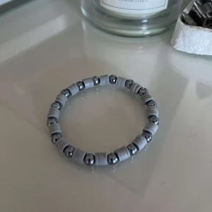 Grått armband med metallpärlor - Säljer ett stilrent grått armband med glänsande metallpärlor. Armbandet har en elastisk tråd som gör det enkelt att ta på och av. Perfekt för både vardag och fest!