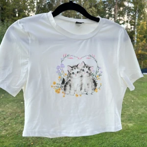 Vit crop top - En vit crop top med ett gulligt katt-tryck på framsidan 🐱🩷 Säljer pga att den inte kommer till användning längre.  Storlek M men passar mig bra som brukar ha S!  (Lite luddig på bilderna)  Längd: 39 cm Axel: 35 cm Byst: 83 cm