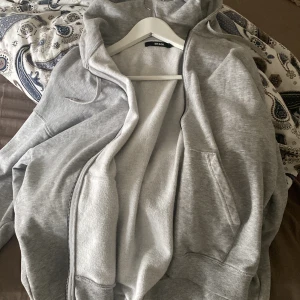 Grå hoodie från Bik Bok - Säljer en supermysig oversized grå hoodie från Bik Bok i storlek XS. Den har en dragkedja framtill. Perfekt för alla dagar. Andvänd få gånger och tyget är som nytt, jätte skön och varm. Passar till allt!