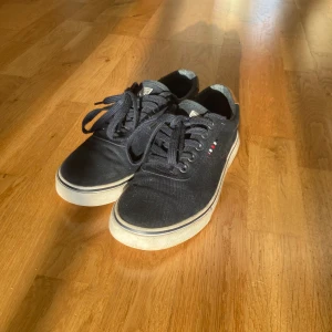 Svarta sneakers med snörning - Säljer ett par mörk blå sneakers i välanvänt skick. De har en klassisk design med snörning och en vit sula som ger en snygg kontrast. Perfekta för vardagsbruk och passar till det mesta i garderoben. Sulan är lite smutsig av röd grus men syns det lite