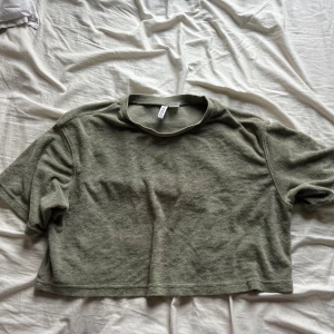 Grön frottétopp - Säljer en grön frottétopp i storlek M. Den är kortärmad och har en croppad passform, perfekt för en avslappnad sommarlook. Toppen är i bra skick och supermjuk!