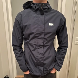 Mörkblå Vind/Regnjacka Helly Hansen - Fin och praktisk jacka. Sparsamt använd och i mycket gott skick. Storlek XS. Normal i storleken.   Tveka inte på att ställa frågor eller be om fler bilder. 