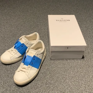 Valentino Garavani sneakers med blå detalj - Säljer ett par snygga Valentino Garavani sneakers i vitt skinn med en cool blå detalj över snörningen. Skorna är i nyskick och kommer med originalförpackning och dustbag. Perfekta för både vardag och fest! 🕺Skickas efter 24 timmar🚚Nypris 7999 kr