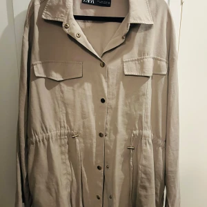 Beige kavaj - Säljer en beige lång kavaj från Zara i storlek M som även kan passa storlek L. Den har en klassisk design och en elegant passform. Kavajen har guldiga knappar och några fickor och är i bra mycket skick och redo för nya äventyr!