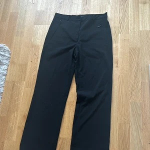 Svarta kostymbyxor från Brandtex - Säljer ett par klassiska svarta kostymbyxor från Brandtex i storlek 38. De har en elegant och tidlös design med en rak passform. Perfekta för både kontoret och festliga tillfällen. Byxorna är i fint skick och redo för en ny ägare!